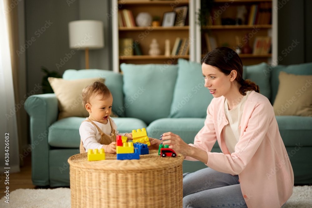 Obraz premium Mother and her baby boy playing with colored toy blocks at home