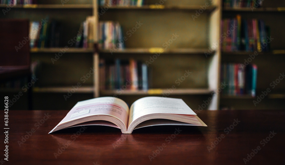 On a wooden table, there's an open book with a library visible in the background. A stack of books nearby adds to the theme of educational learning. On a wooden table, there's an open book with a library visible in the background. A stack of books nearby adds to the theme of educational learning.