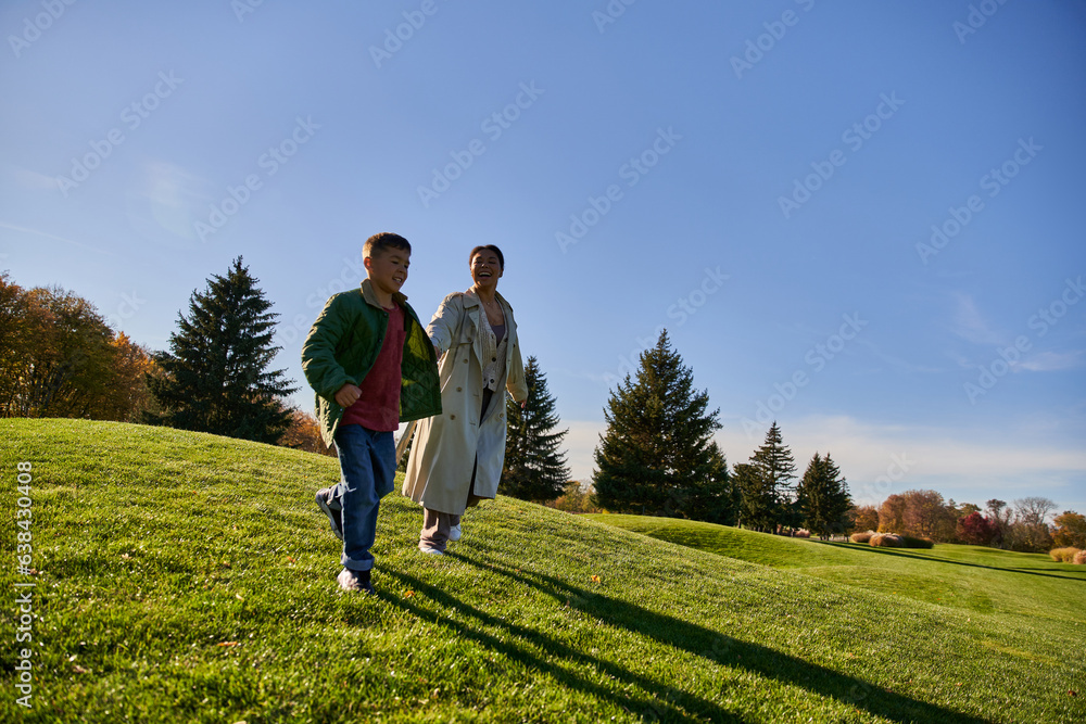 sunny day in autumn, cheerful african american woman running together with son in park, candid sunny day in autumn, cheerful african american woman running together with son in park, candid