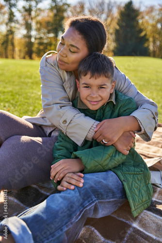 bonding and love, mother hugging son, happy african american woman and boy in outerwear, fall season © LIGHTFIELD STUDIOS