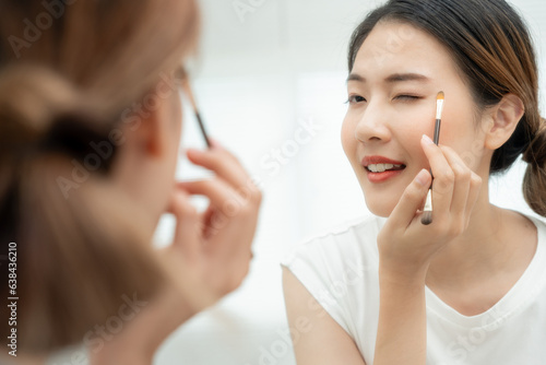 Beautiful Asian woman sit in front of a mirror and smile on makeup. face of a healthy woman applying makeup. Advertisement  lifestyle   cosmetics  makeup accessories  beauty activity  beautician