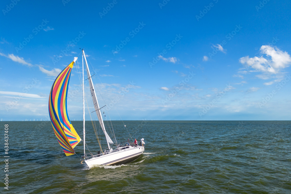 Naklejka premium Drone shot of a sailboat healed over with bright colourful genoa, gennaker, or asymmetric spinnaker headsail in windy conditions under blue sky in The Netherlands