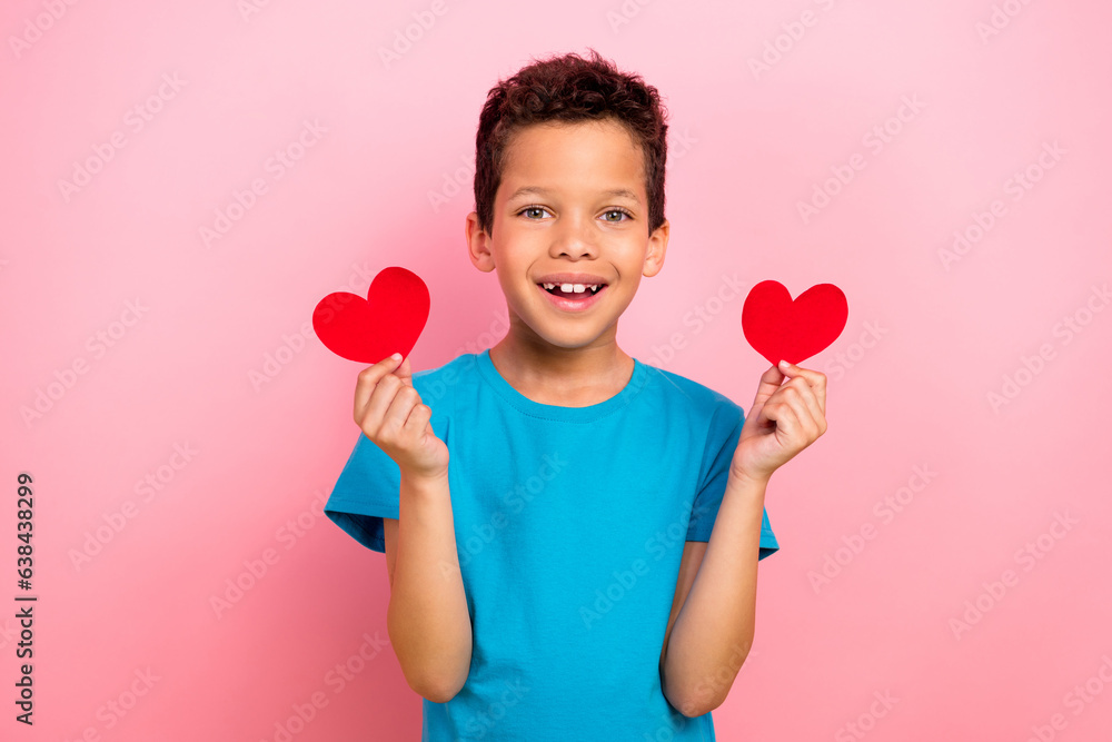 Photo portrait of charming small boy hold two red heart postcards wear trendy blue garment isolated on pink color background Photo portrait of charming small boy hold two red heart postcards wear trendy blue garment isolated on pink color background