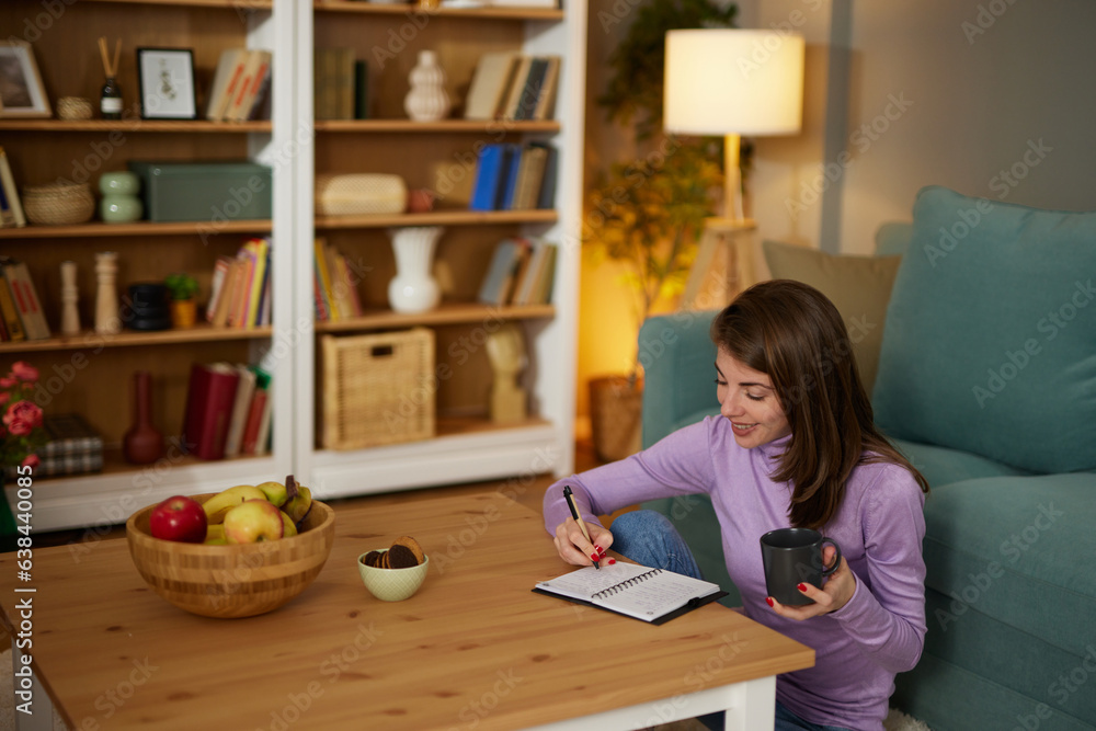 Pretty young woman sitting in cozy living room and making notes to her diary Pretty young woman sitting in cozy living room and making notes to her diary