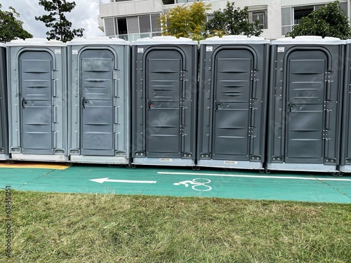 A row of portable toilets outdoors by a bicycle road in a park. photo