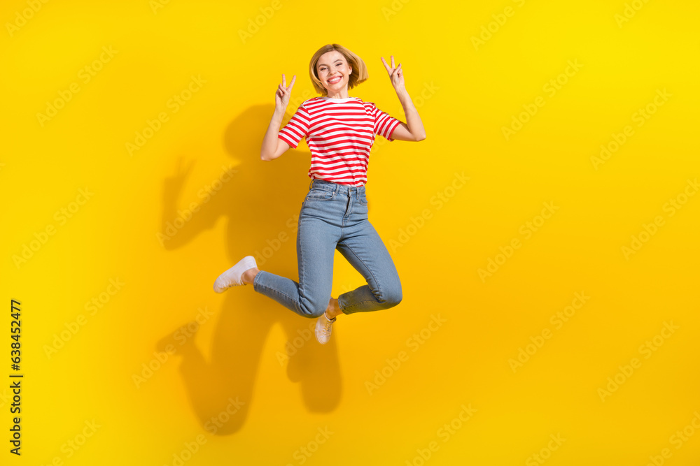 Full body photo of carefree excited lady jumping demonstrate v-sign empty space isolated on yellow color background Full body photo of carefree excited lady jumping demonstrate v-sign empty space isolated on yellow color background