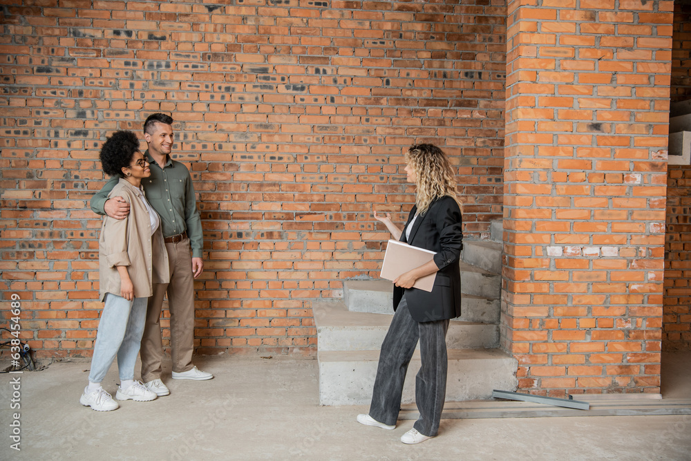 real estate broker with folder showing unfinished interior of new house to interracial couple real estate broker with folder showing unfinished interior of new house to interracial couple