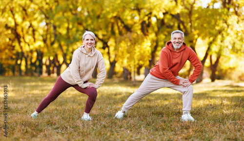 Happy smiling mature man and woman in sportswear stretching body while warming up together outdoors.