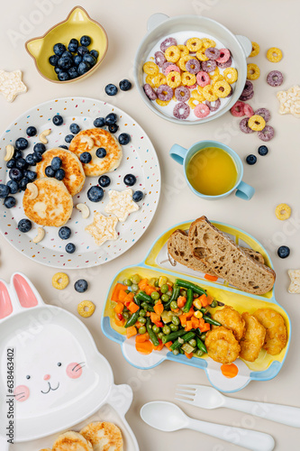 Cute plates with a variety of children's food. Vegetables, nuggets, french fries, pancakes, cereal and juice. Creative serving for baby. Concept of kids menu, nutrition and feeding.