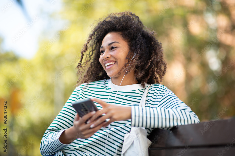 smiling young woman sitting with cellphone on park bench smiling young woman sitting with cellphone on park bench