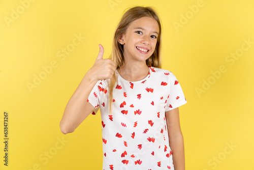 Beautiful teen girl doing happy thumbs up gesture with hand. Approving expression looking at the camera showing success. photo