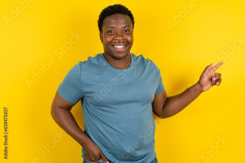 Young handsome man standing over yellow studio background looking at camera indicating finger empty space sales