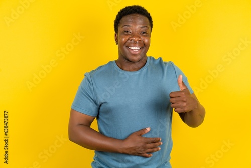 Young handsome man standing over yellow studio background happy positive smile hands on belly show thumb-up fine healthy