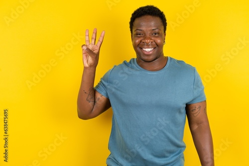 Young handsome man standing over yellow studio background showing and pointing up with fingers number three while smiling confident and happy. photo