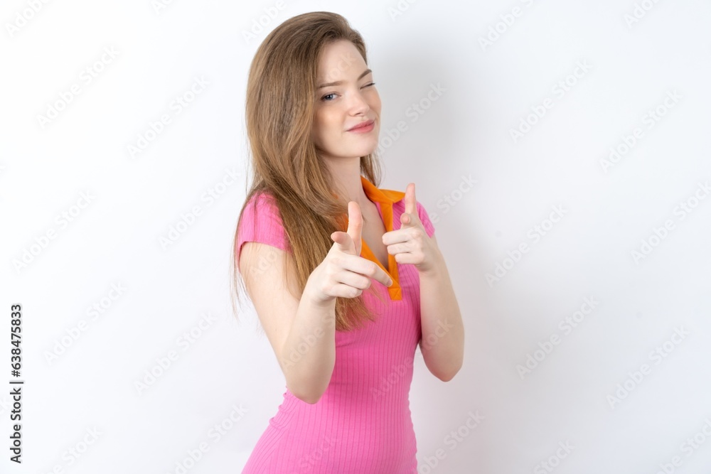 Joyful young beautiful red haired woman wink and points index fingers at camera, chooses someone, makes finger gun pistol. Joyful young beautiful red haired woman wink and points index fingers at camera, chooses someone, makes finger gun pistol.