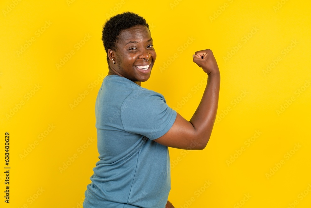 Fototapeta premium Portrait of powerful cheerful handsome African American standing over yellow studio background showing muscles.