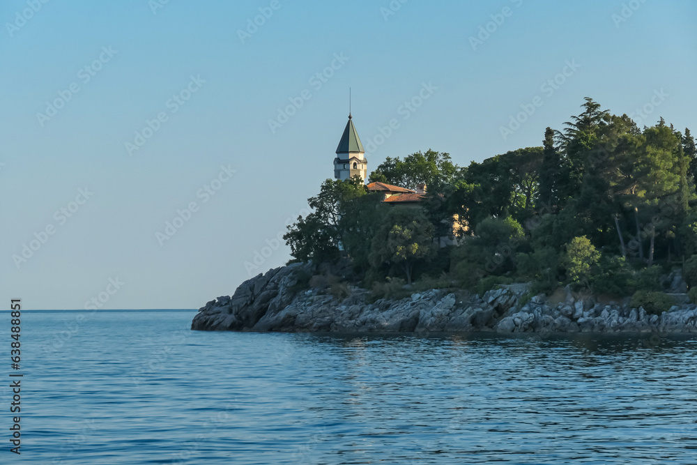 A close up on a tower between the trees along the shore of Medveja, Croatia. The Mediterranean Sea is calm and clear. Steep and stony shores of the sea. Clear sky. Summer remedy. An island in the back