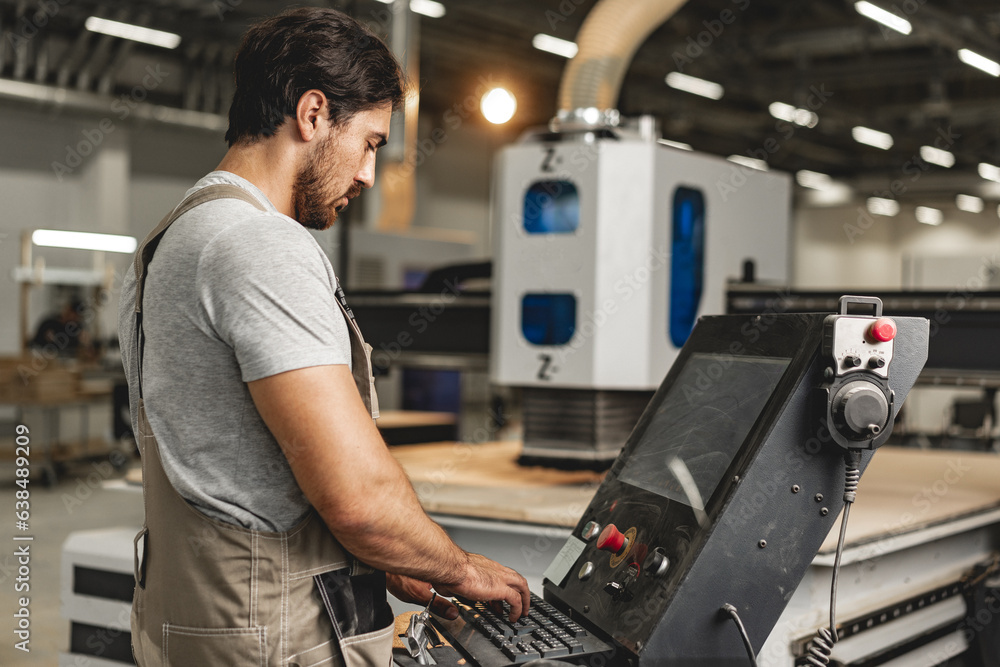 Young carpenter operating machine for wood processing at a furniture factory Young carpenter operating machine for wood processing at a furniture factory