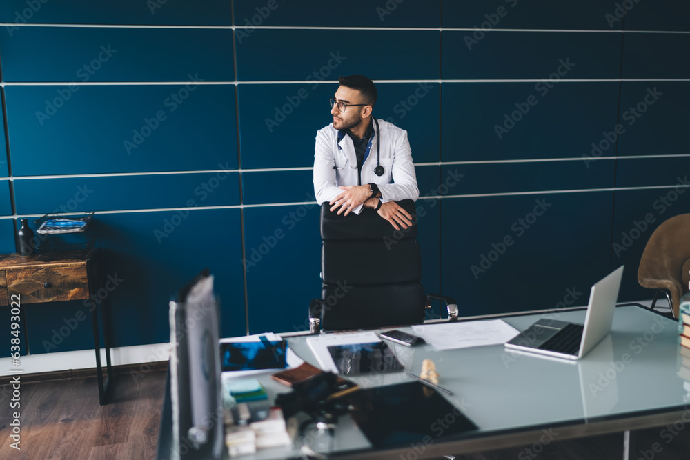 Pensive male doctor standing in office during break Pensive male doctor standing in office during break