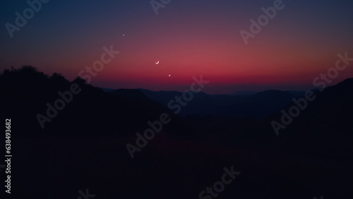 Silhouette of a countryside with Milky Way stars, planets and crescent Moon.