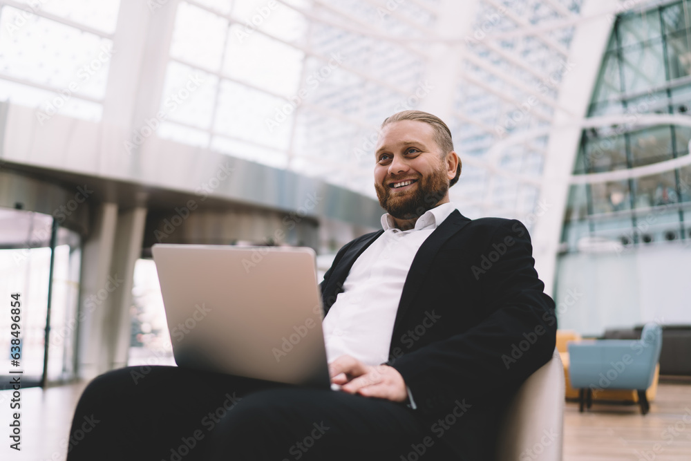 Cheerful businessman sitting with laptop in spacious hall Cheerful businessman sitting with laptop in spacious hall