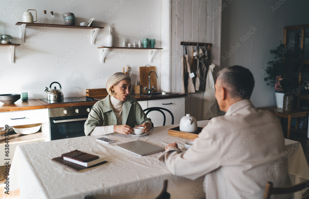Mature couple talking at kitchen table with cups of mug Mature couple talking at kitchen table with cups of mug