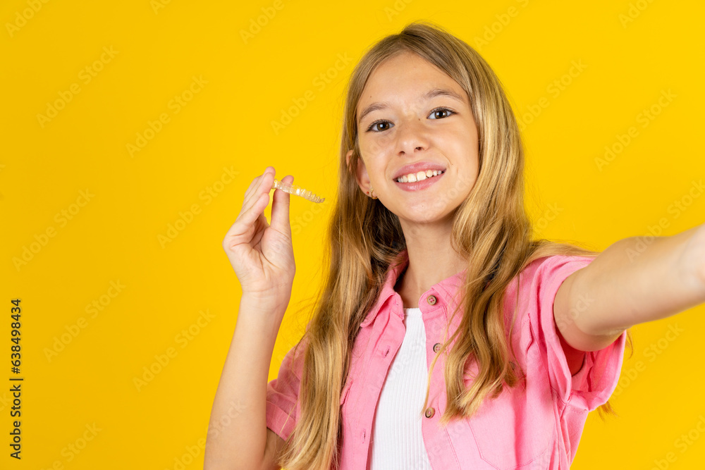 Beautiful caucasian kid girl wearing pink shirt make selfie holding an invisible braces aligner, recommending this new treatment. Dental healthcare concept. Beautiful caucasian kid girl wearing pink shirt make selfie holding an invisible braces aligner, recommending this new treatment. Dental healthcare concept.