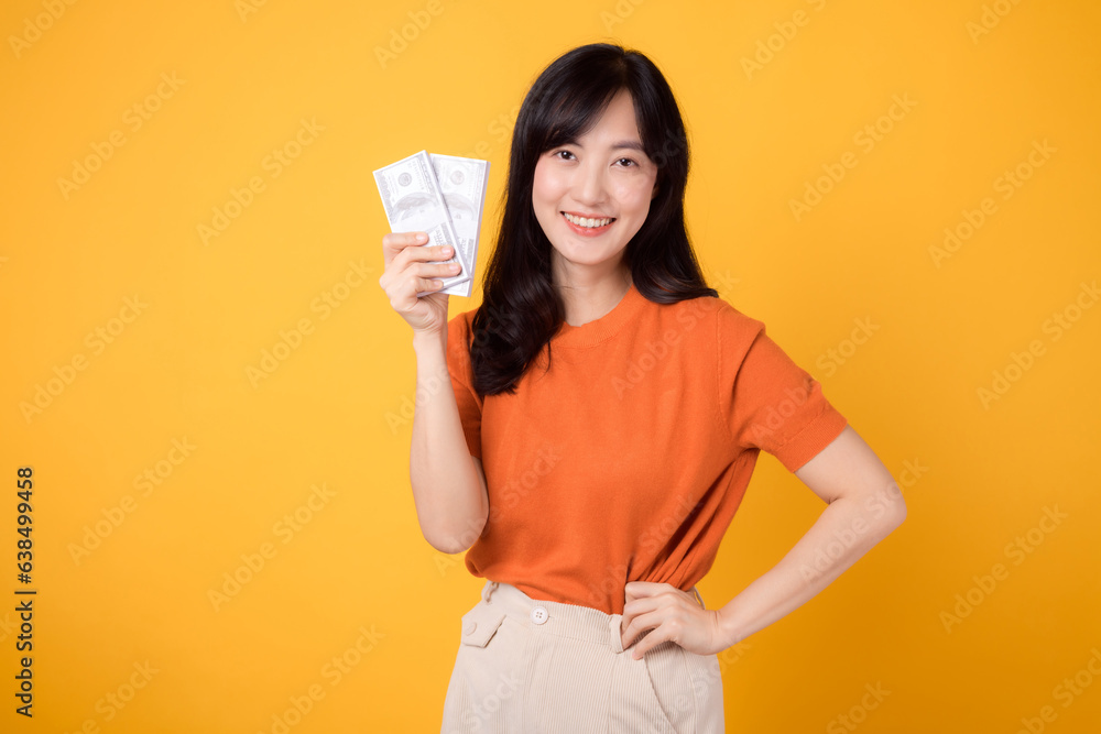 Dynamic young Asian woman in her 30s, holding cash money dollars, standing on vibrant yellow backdrop. Dynamic young Asian woman in her 30s, holding cash money dollars, standing on vibrant yellow backdrop.