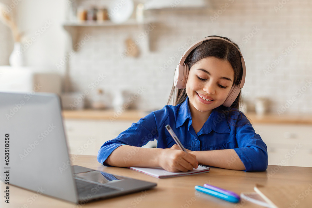 Cheerful girl studying online using laptop and headset indoor Cheerful girl studying online using laptop and headset indoor