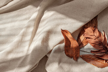 Messy brown fall leaves on neutral beige linen crumpled fabric background with aesthetic natural sunlight shadows. Lifestyle boho business brand template