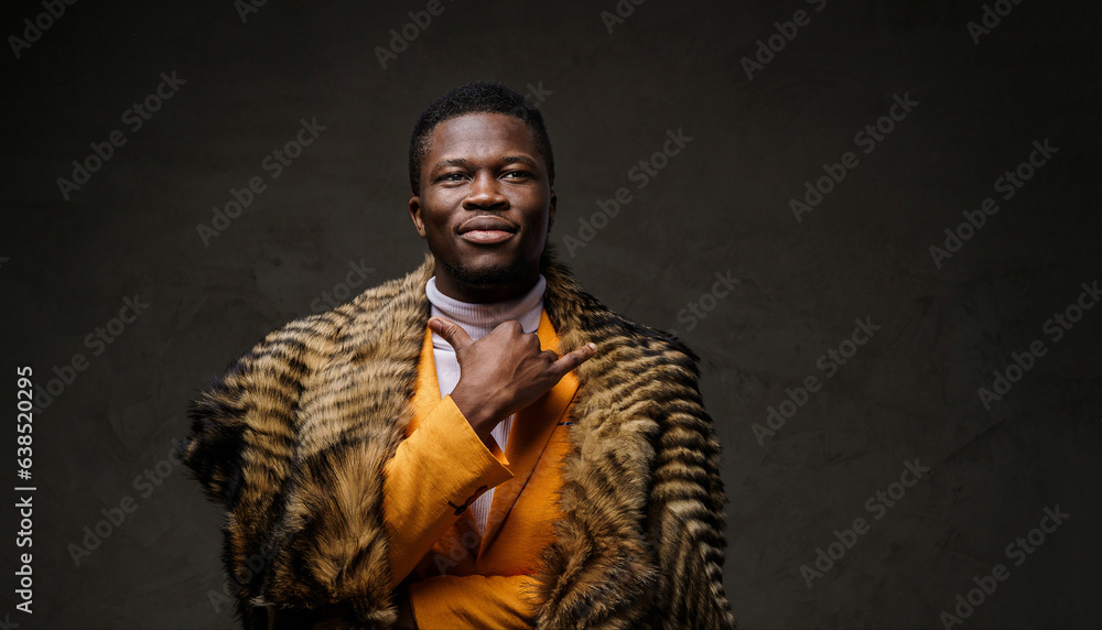 A stylish, dark-skinned man wearing a yellow jacket and a wild animal fur poses while gesturing Shaka confidently against a textured dark background A stylish, dark-skinned man wearing a yellow jacket and a wild animal fur poses while gesturing Shaka confidently against a textured dark background