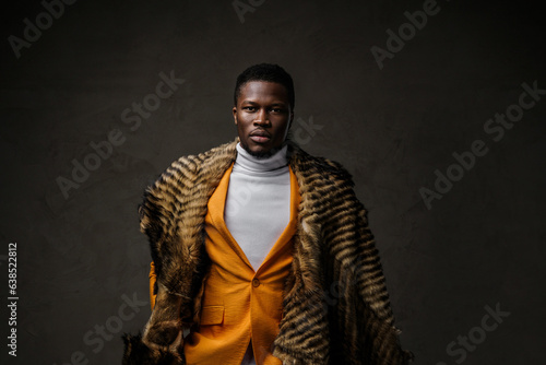 Bold and fashionable portrait of a dark-skinned male donning a striking yellow blazer, embellished with a draped animal fur and set against a dark backdrop