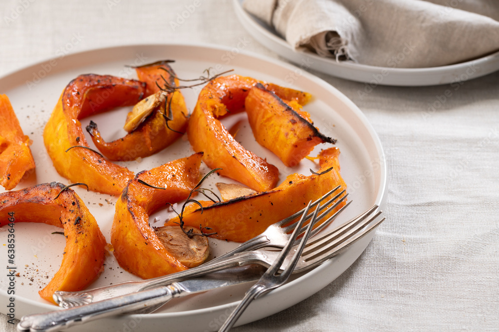 pieces of baked pumpkin with spices and garlic on a beige plate and beige background pieces of baked pumpkin with spices and garlic on a beige plate and beige background