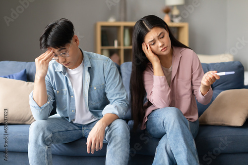 Upset asian couple with negative pregnancy test sitting at home photo