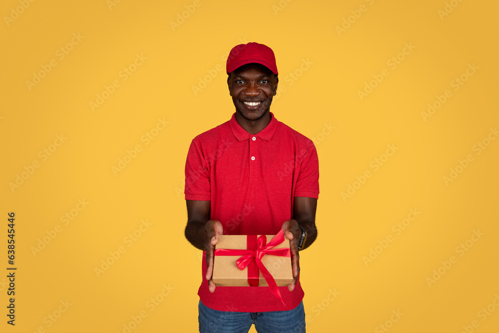 Happy millennial african american guy courier in uniform gives box gift Happy millennial african american guy courier in uniform gives box gift