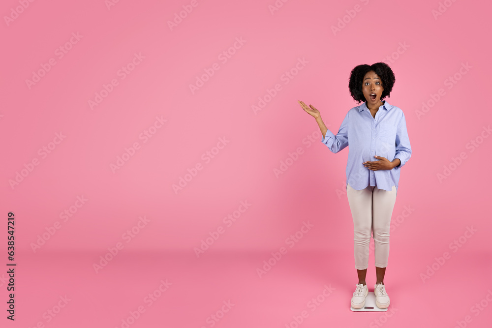 Glad shocked young black pregnant lady in casual touching big belly with hand, pointing finger at copy space Glad shocked young black pregnant lady in casual touching big belly with hand, pointing finger at copy space