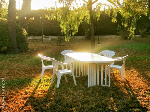 Mesa blanca con cinco sellas blancas sobre césped verde en un jardín idílico al amanecer.