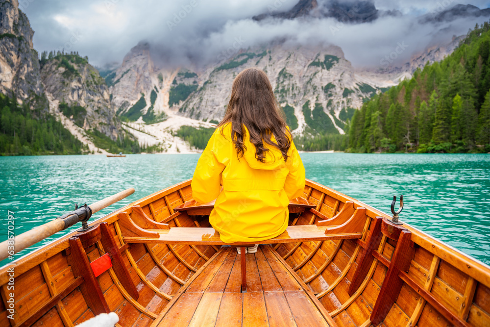 Woman sitting in big brown boat at Lago Braies lake in cloudy day, Italy. Summer vacation in Europe