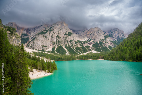 Braies lake surrounded by pine forests and the rocky ranges of the Dolomites in cloudy day, Italy.