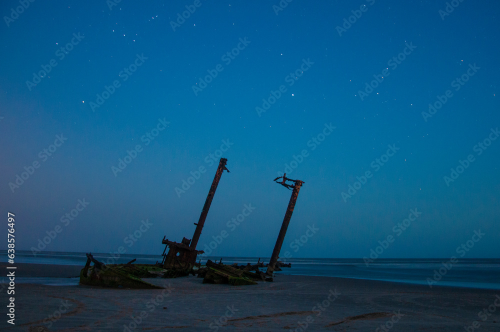 Night sky with stars and a shipwreck on the beach. Long exposure.