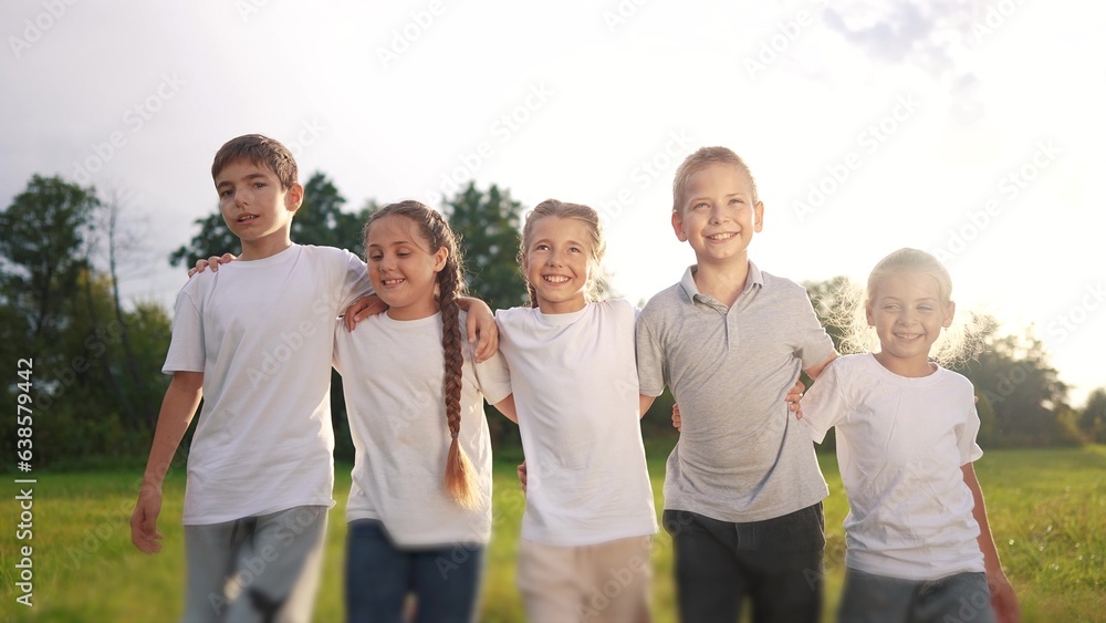 a group of children walk on the grass in the park hugging each other. happy family childhood dream concept. little kids are smiling and lifestyle walking across the field on the grass at sunset