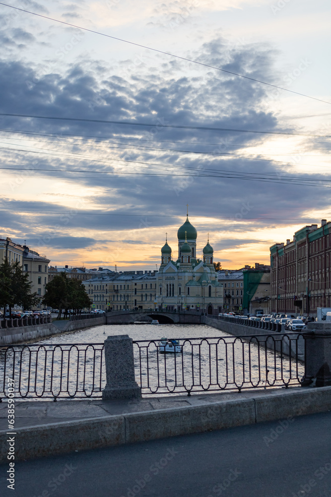 Panorama of St.Petersburg at dusk. Orthodox church, Neva river, buildings, bridge, boat, cars on the waterfront. Cloudy sky. Evening.