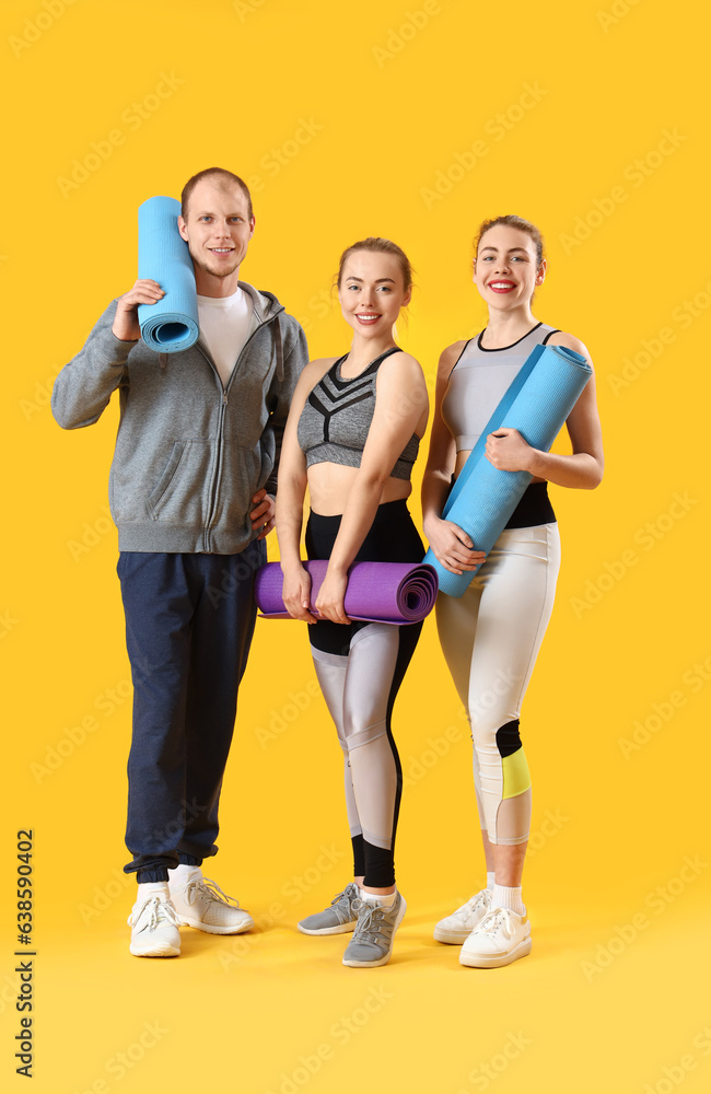 Obraz premium Sporty young people with fitness mats on yellow background
