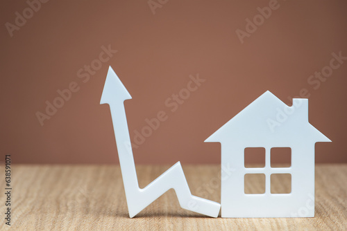 An increase in the interest rate for a mortgage or an increase in the cost of insurance for a property. White house model and graphic arrow pointing up close up on brown background. copy space.