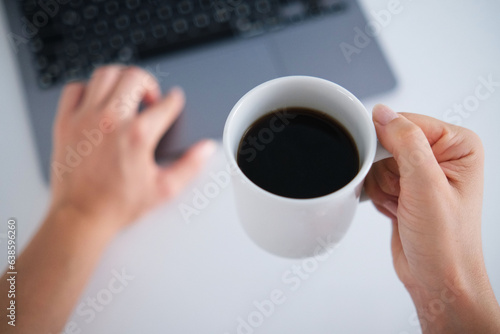 Top view young woman's holding a cup of filter coffee while using laptop.Daily routine, morning person.Coffee day concept.