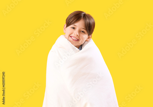 Little boy wrapped in blanket on yellow background