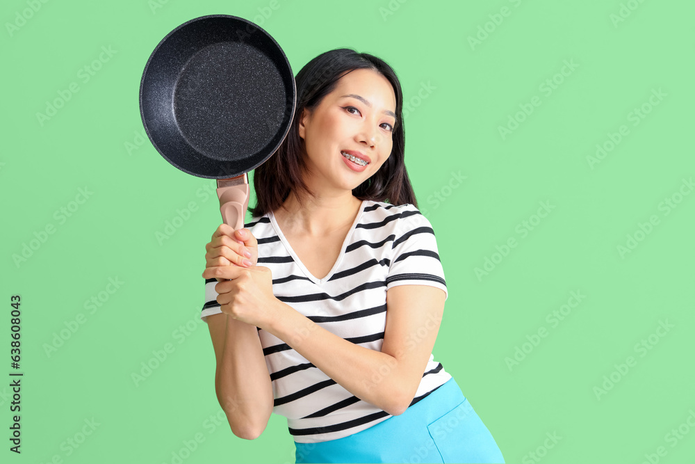 Happy beautiful Asian woman with frying pan on green background Happy beautiful Asian woman with frying pan on green background