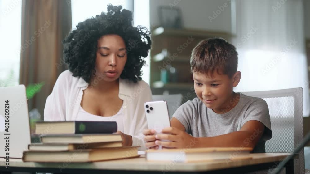Bored primary school boy kid looking at smartphone ignoring mad mother screaming at him because studying at home Angry woman mom doing homework together indoors Children phone addiction concept Bored primary school boy kid looking at smartphone ignoring mad mother screaming at him because studying at home Angry woman mom doing homework together indoors Children phone addiction concept