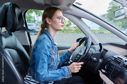 Fotografie Teenage girl driver in glasses sitting behind wheel of car