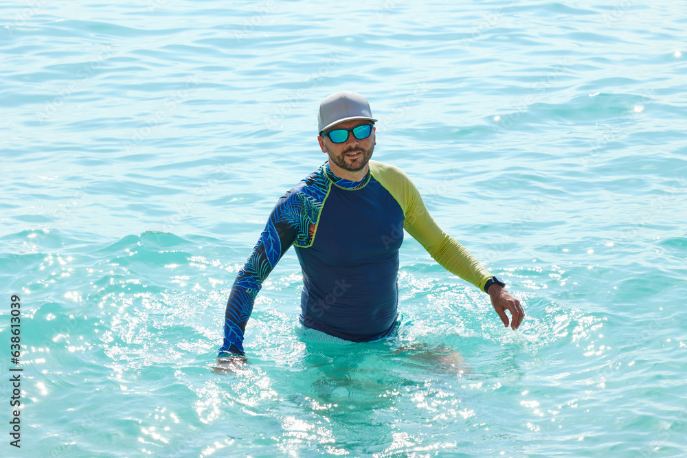 Handsome man standing waist-deep in blue sea water.